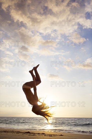 Silhouette of mixed race woman doing backflip on beach
