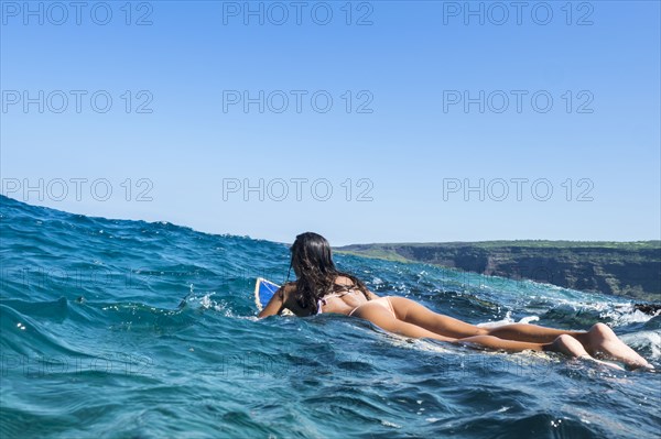 Mixed race woman laying on surfboard in ocean waves