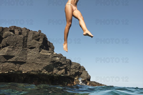 Mixed race woman jumping from rocks into ocean