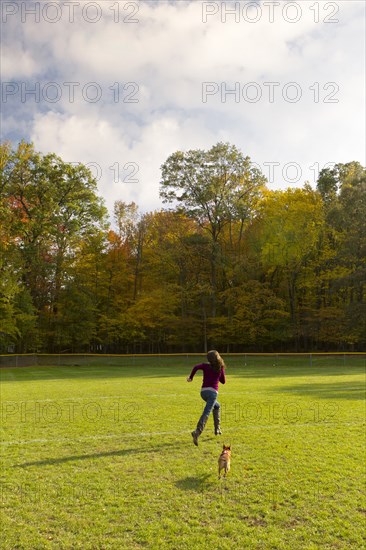 Caucasian woman running with dog in field