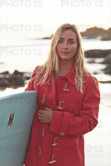 Caucasian woman in coat carrying surfboard on beach