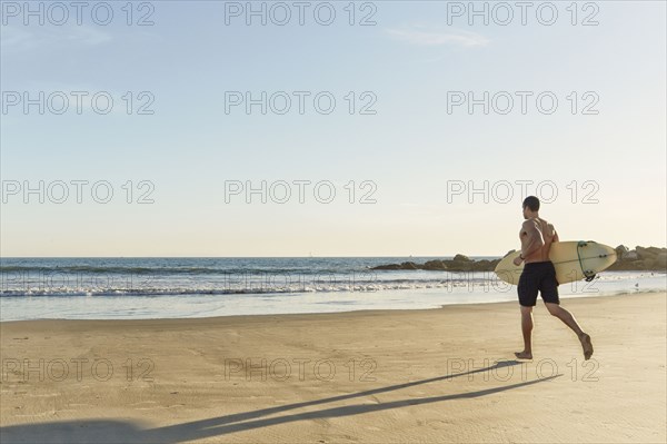 Mixed race man running with surfboard on beach