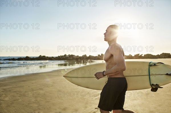 Mixed race man running with surfboard on beach