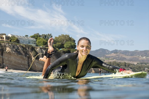 Smiling Caucasian woman paddling on surfboard in ocean