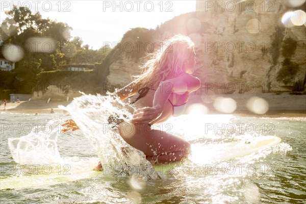 Caucasian woman kneeling on surfboard in ocean and paddling