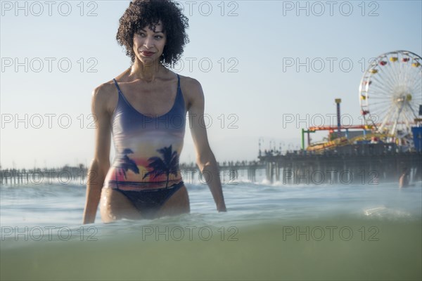 Mixed Race woman wading in ocean near amusement park