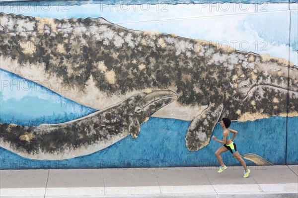 Distant Mixed Race woman running on sidewalk near mural