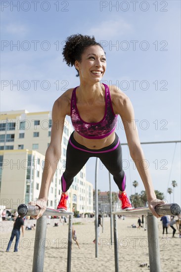 Mixed Race woman balancing on parallel bars at beach