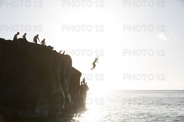 Friends jumping from cliff into ocean