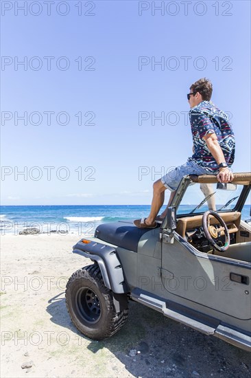 Caucasian man sitting in windshield of convertible car on beach