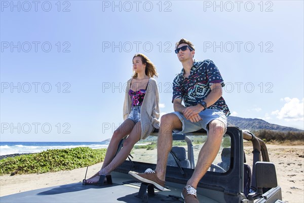 Couple sitting on windshield of convertible car on beach