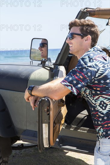 Reflection of Caucasian man in side-view mirror of car on beach