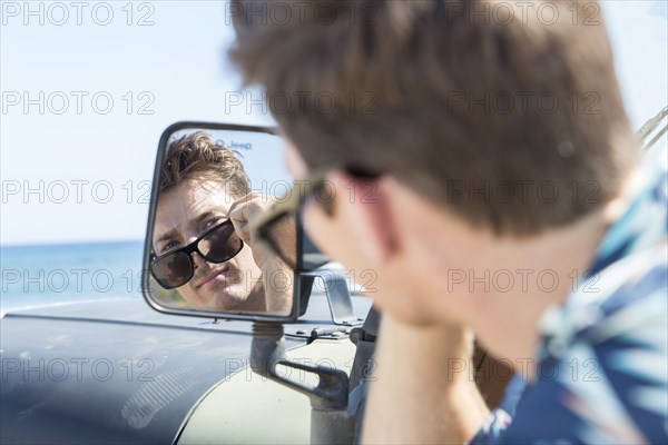 Reflection of Caucasian man in side-view mirror of car on beach