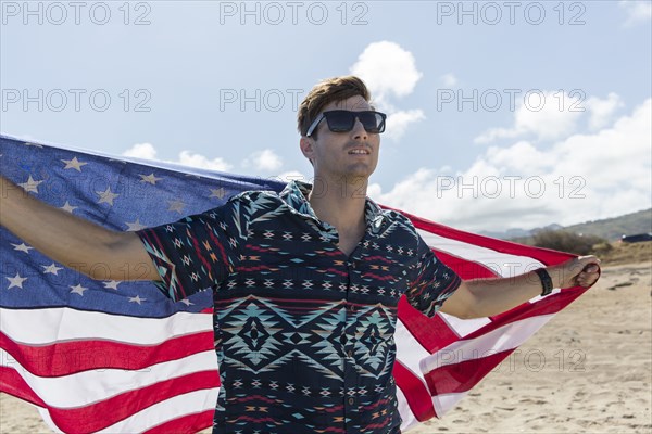 Caucasian man holding American flag on beach