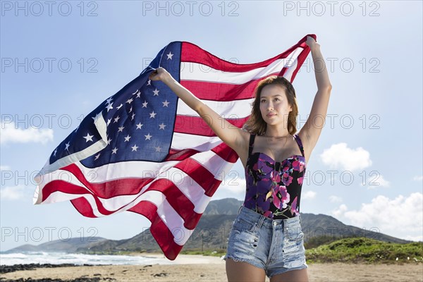 Mixed Race woman holding American flag on beach