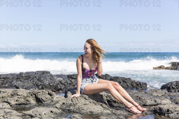 Mixed Race woman sitting on rocks at beach