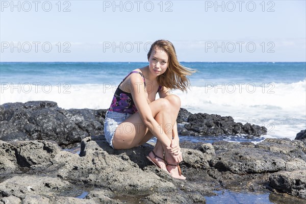 Portrait of serious Mixed Race woman sitting on rocks at beach