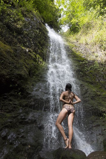 Caucasian woman standing on rock near waterfall performing yoga