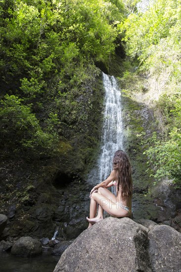 Caucasian woman sitting on rock near waterfall