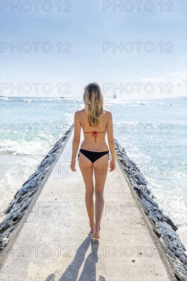 Caucasian woman wearing bikini walking on breakwall