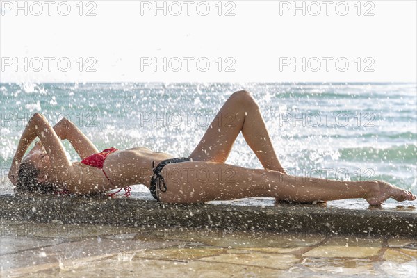 Ocean waves splashing on Caucasian woman wearing bikini