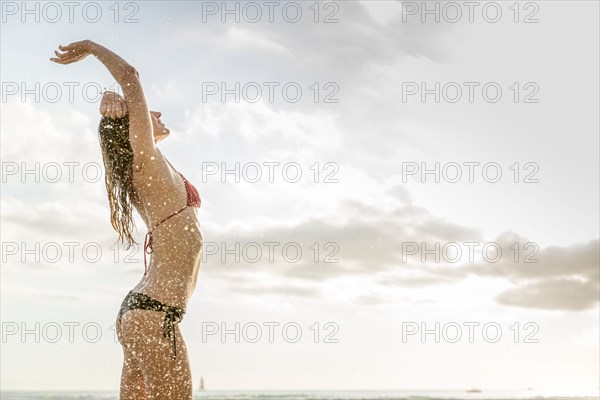 Ocean waves splashing on Caucasian woman wearing bikini