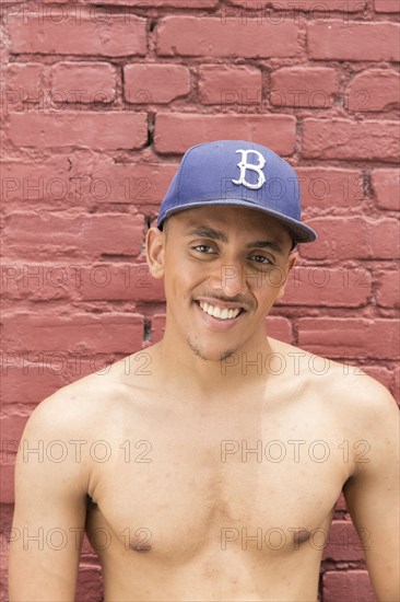 Portrait of shirtless Mixed Race man wearing hat near brick wall