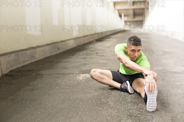 Mixed Race man sitting on ground stretching leg