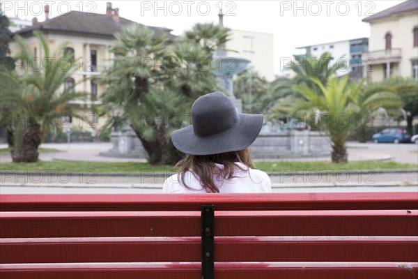 Woman wearing sun hat sitting on red bench