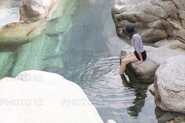 Woman wearing sun hat dangling feet in river