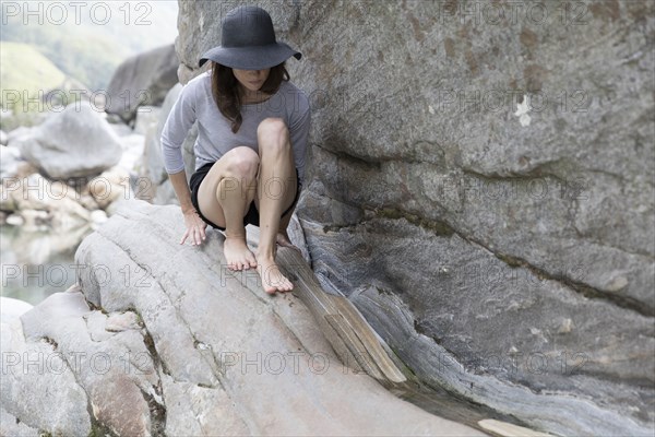 Woman wearing sun hat crouching on rock