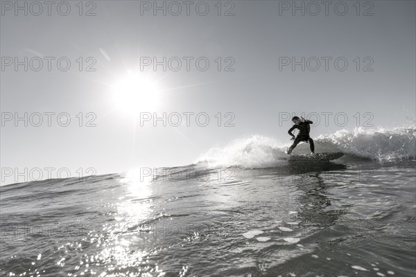 Distant Caucasian man surfing in sunny ocean