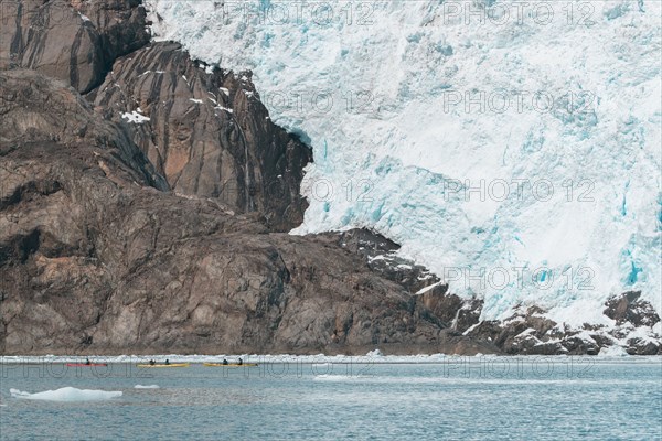 Distant people kayaking near glacier