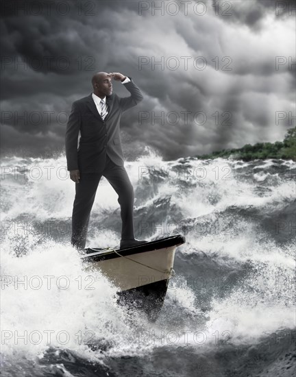 African American businessman standing at helm of boat on stormy sea