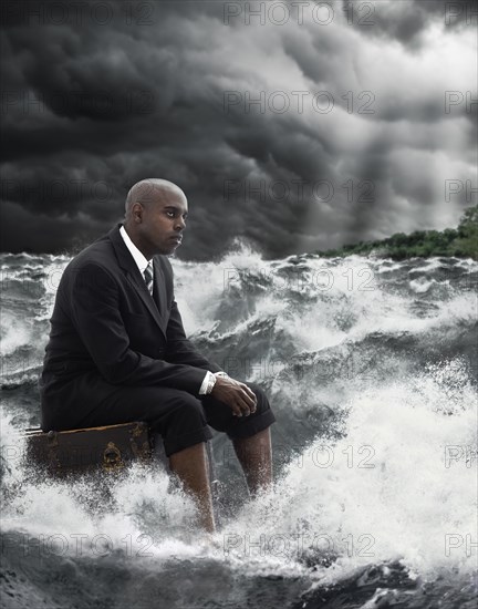 African American businessman sitting on suitcase in stormy sea