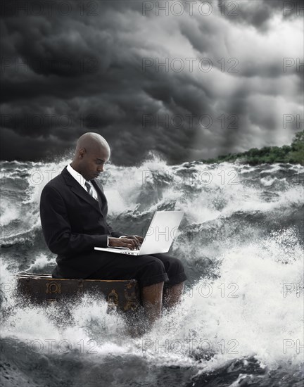 African American businessman using laptop in stormy sea