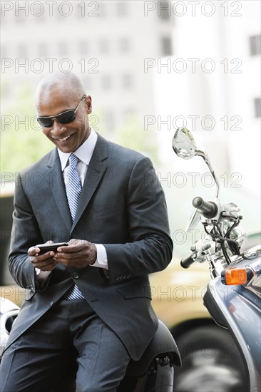 Black businessman sitting on scooter text messaging