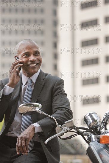 Black businessman sitting on scooter talking on cell phone