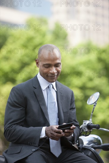 Black businessman sitting on scooter text messaging