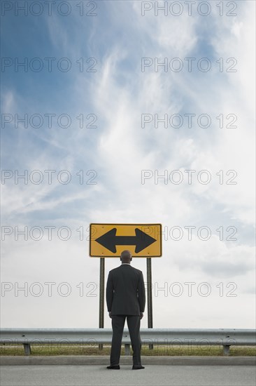 African American businessman looking at conflicting road sign