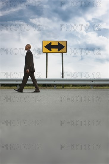 African American businessman walking on road near road sign