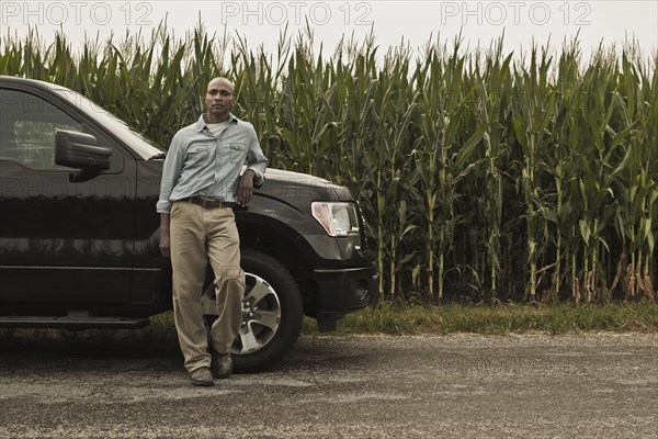 African American farmer leaning on car next to crop