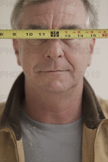 Caucasian carpenter covering eyes with measuring tape