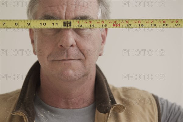Caucasian carpenter covering eyes with measuring tape