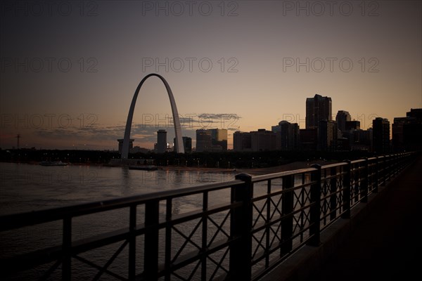 Arch landmark next to urban river at sunset