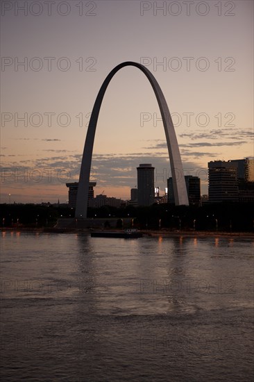 Arch landmark next to urban river at sunset