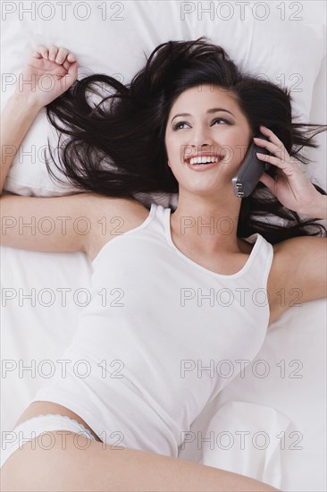 Alluring mixed race woman laying in bed talking on telephone