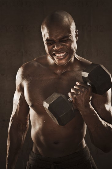 Grimacing African American man lifting weights