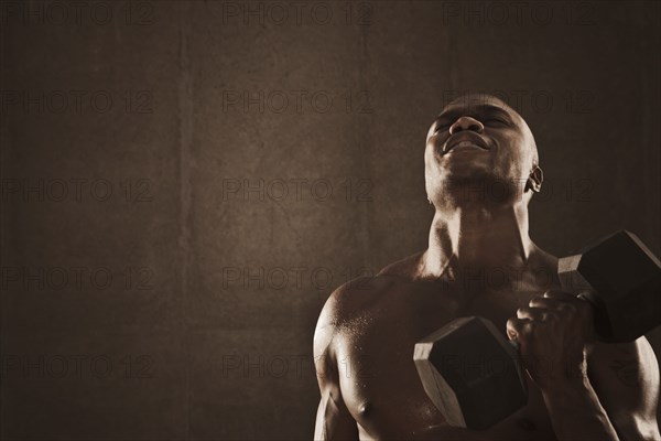 Grimacing African American man lifting weights