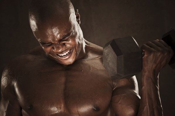 Grimacing African American man lifting weights